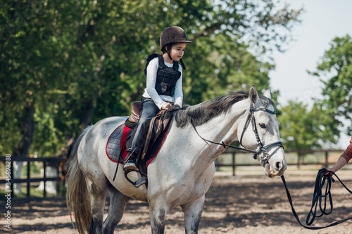 Little Girl in helmet Learning Horseback Riding. Instructor teaches kid Equestrian. © sergiophoto