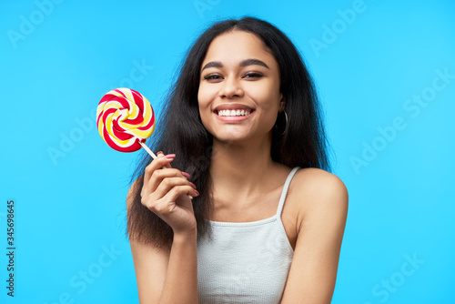 Happy beautiful black woman with colorful lollipop on blue background © GVS