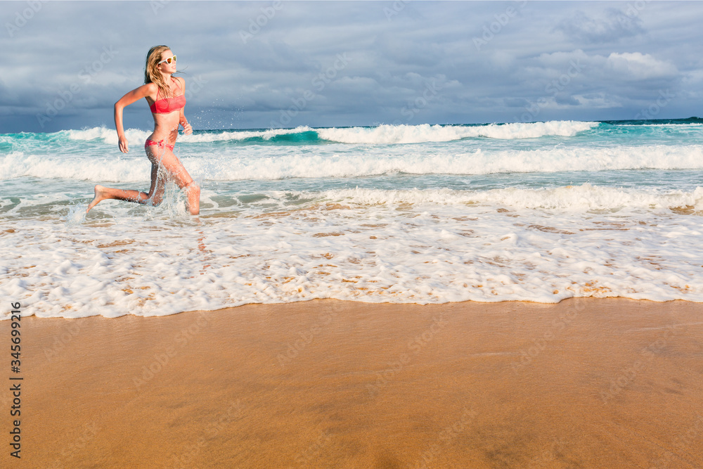 Beautiful blonde woman in bikini running in the water on tropical beach. Portrait of happy young sporty woman.