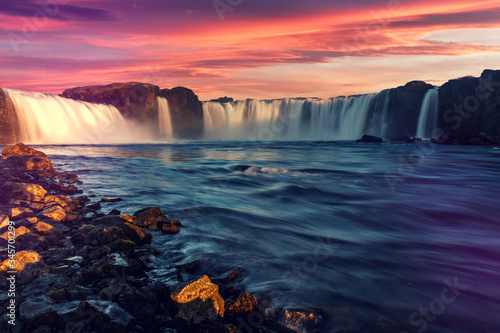 Colorful summer landscape of Iceland. Majestic Godafoss waterfall with picturesque dramatic sky  during sunset. Scenic image of Icelandic nature.  Popular travel and hiking destination