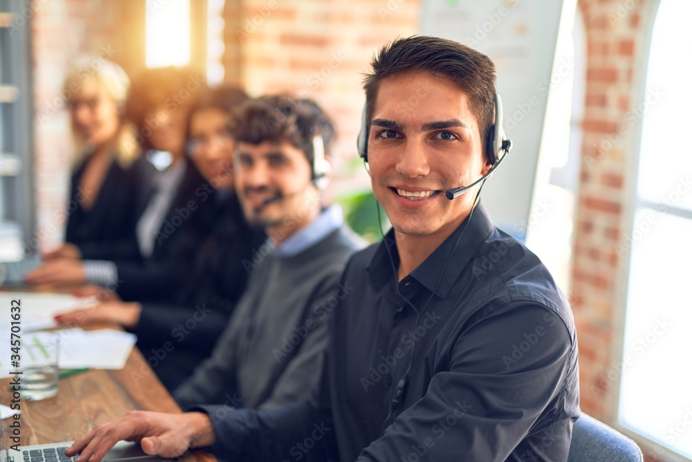 Group of call center workers working together with smile on face using headset. Young handsome man smiling at the office. Group of call center workers working together with smile on face using headset. Young handsome man smiling at the office.