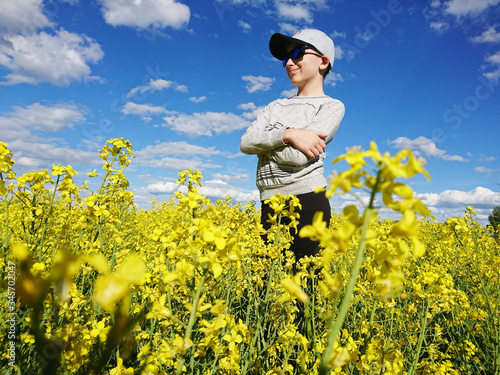 chłopczyk w czapeczce i w okularach stojący w polu kwitnącego rzepaku 