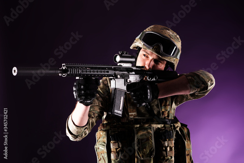 Soldier with gun is looking through the scope on violet background. Concept of war. Veterans, comrades, soldiers. Man in uniform. photo