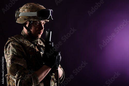 Soldier with gun aims at the target on mission on violet background. Concept of war. photo