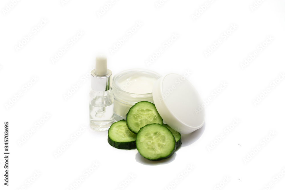 A cosmetic bottle and an opened jar of facial or body cream with many sliced cucumbers on the white background. Natural cosmetics. A cosmetic bottle and an opened jar of facial or body cream with many sliced cucumbers on the white background. Natural cosmetics.