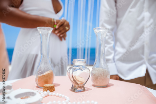  Bride and groom pouring colorful different colored sands into the crystal vase close up during symbolic nautical decor destination wedding marriage ceremony on sandy beach in front of the ocean