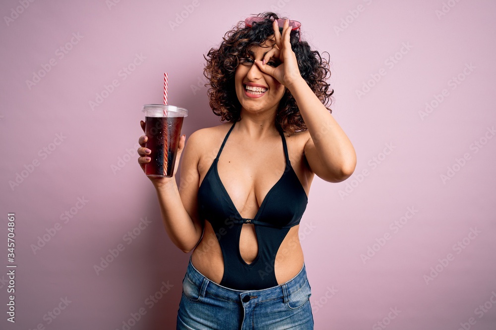 Beautiful arab woman on vacation wearing swimsuit drinking cola refreshment using straw with happy face smiling doing ok sign with hand on eye looking through fingers Beautiful arab woman on vacation wearing swimsuit drinking cola refreshment using straw with happy face smiling doing ok sign with hand on eye looking through fingers