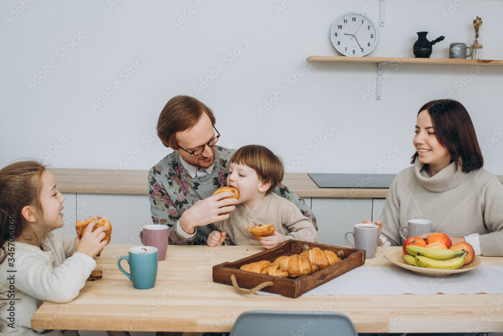 Young happy family with two kids having breakfast together. redheaded dad, kids and brunette mom together in the kitchen. Young happy family with two kids having breakfast together. redheaded dad, kids and brunette mom together in the kitchen.