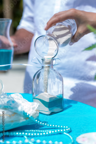 
Bride and groom pouring colorful different colored sands into the crystal vase close up during symbolic nautical decor destination wedding marriage ceremony on sandy beach in front of the ocean