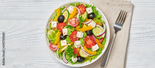 Greek salad with cucumeber, olives, feta cheese, cherry tomatoes, bell pepper and lettuce. Summer diet salad concept. Tasty greek salad in bowl on wood, top view, banner