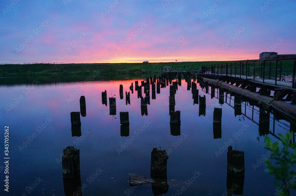 Beautiful violet-blue sunset on a small river wooden posts in the water