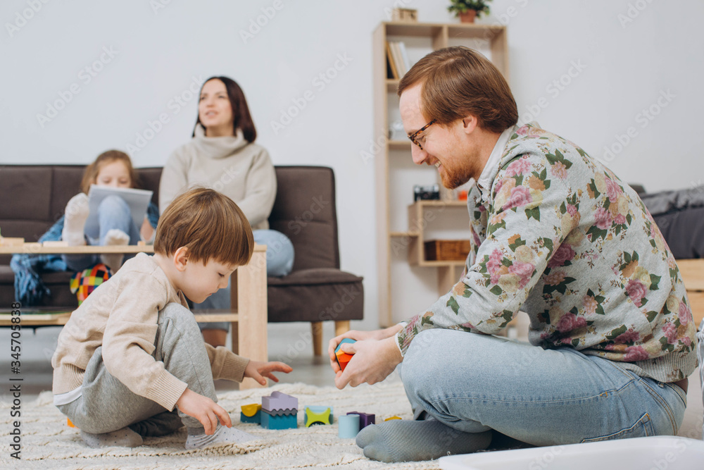 Fototapeta premium Ojciec w okularach i syn uroczego malucha buduje drewnianą wieżę konstruktora.