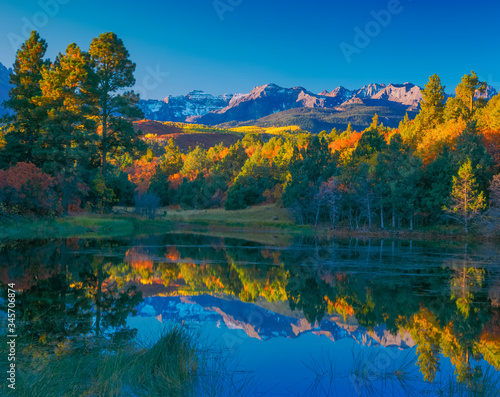 A pond surrounded by fall color reflects the trees and the Sneffels Range mountains in Ridgway, Colorado, USA.  This is in the San Juan Mountains. photo