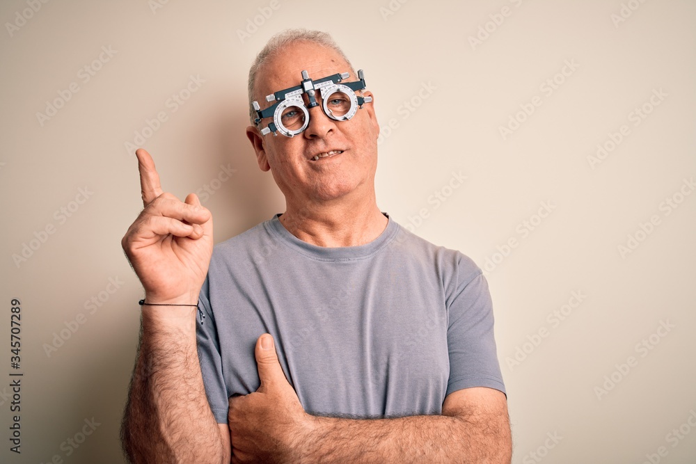 Naklejka premium Middle age hoary man controlling vision wearing optometry glasses over white background with a big smile on face, pointing with hand and finger to the side looking at the camera.