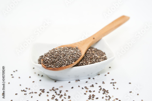 White porcelain bowl and wooden spoon with chia seeds, isolated on white background