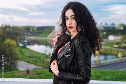 Fashion portrait of sexy beautiful brunette woman with red lipstick wearing a  black leather jacket outdoors in the city