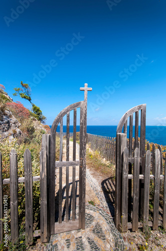 Cliff way around Kolymvaria, Greece. The narrow path winds along the steep cliffs. A gate allows the hiker to a small chapel.