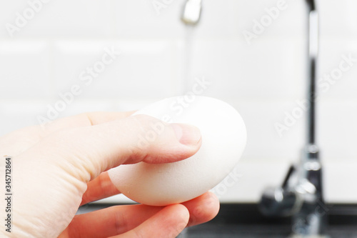 Wash a chicken egg under running water in the kitchen in the sink