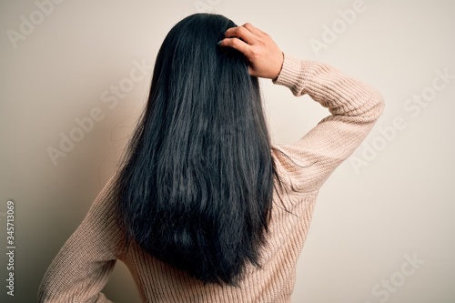 Young beautiful chinese woman wearing casual sweater over isolated white background Backwards thinking about doubt with hand on head