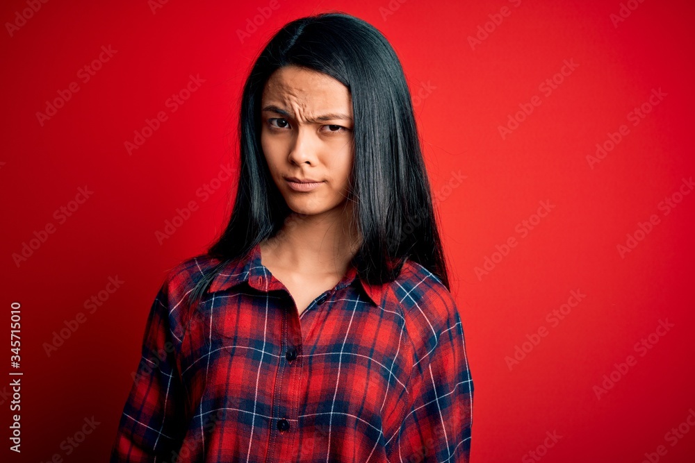 Young beautiful chinese woman wearing casual shirt over isolated red background skeptic and nervous, frowning upset because of problem. Negative person. Young beautiful chinese woman wearing casual shirt over isolated red background skeptic and nervous, frowning upset because of problem. Negative person.