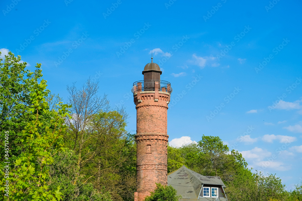 old red brick tower or lookout tower between green trees and blue sky in the background