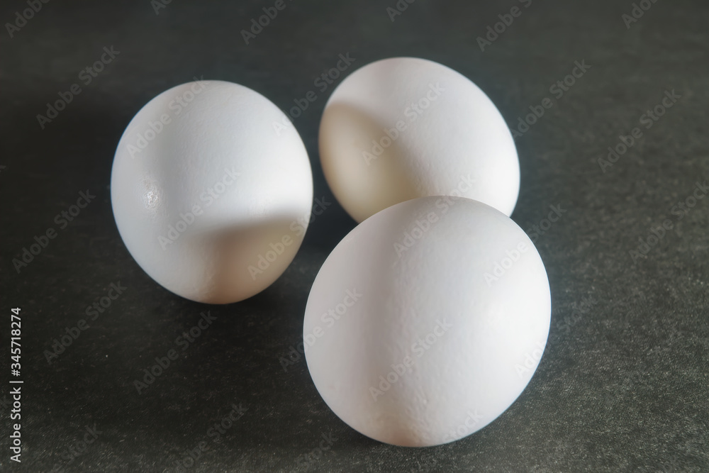 Three white chicken eggs on a dark background close-up. Three white chicken eggs on a dark background close-up.