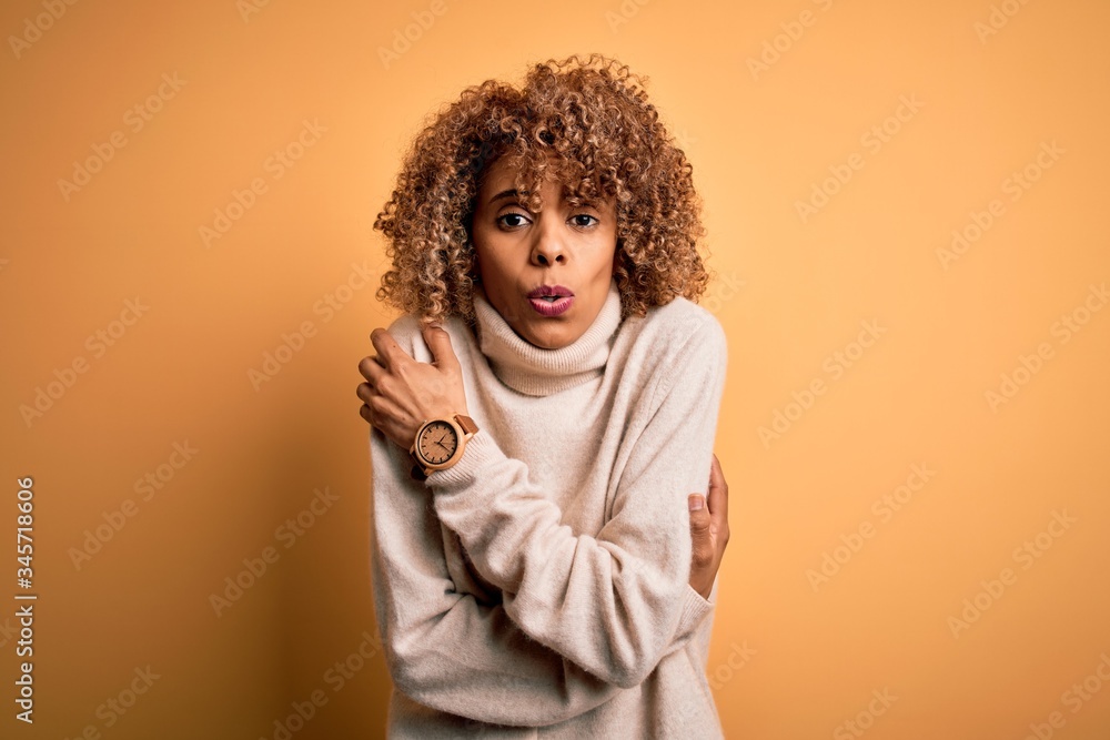Young beautiful african american woman wearing turtleneck sweater over yellow background shaking and freezing for winter cold with sad and shock expression on face Young beautiful african american woman wearing turtleneck sweater over yellow background shaking and freezing for winter cold with sad and shock expression on face