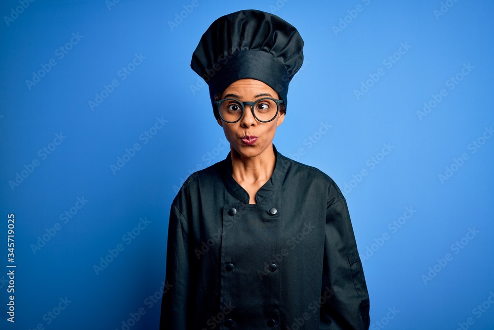 Young african american chef woman wearing cooker uniform and hat over blue background making fish face with lips, crazy and comical gesture. Funny expression. Young african american chef woman wearing cooker uniform and hat over blue background making fish face with lips, crazy and comical gesture. Funny expression.