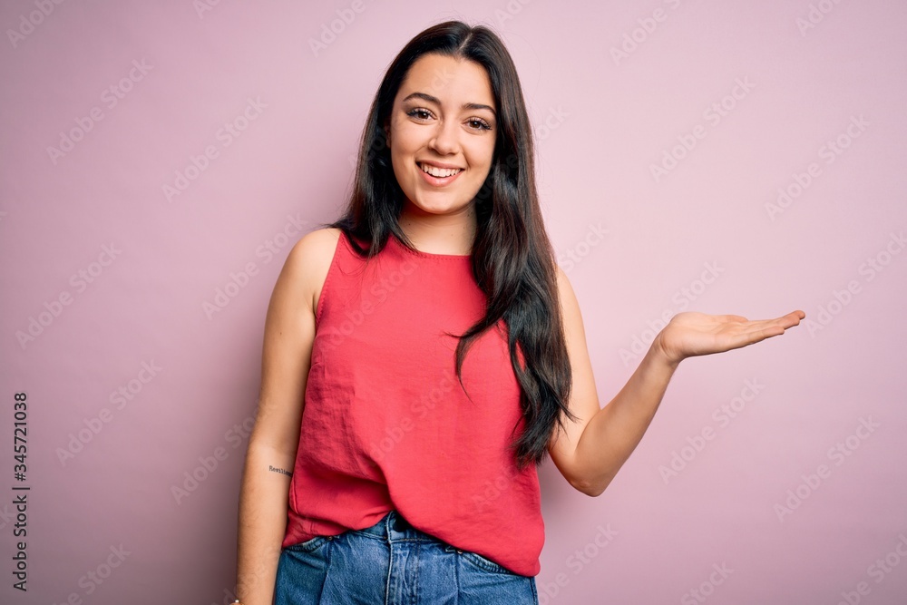 Young brunette woman wearing casual summer shirt over pink isolated background smiling cheerful presenting and pointing with palm of hand looking at the camera. Young brunette woman wearing casual summer shirt over pink isolated background smiling cheerful presenting and pointing with palm of hand looking at the camera.