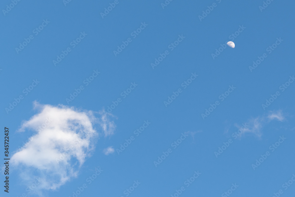 The half moon surround by clouds in the bright blue daytime sky. The half moon surround by clouds in the bright blue daytime sky.