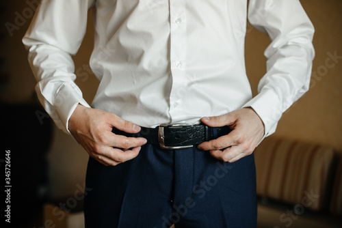 A stylish man puts on a leather belt close-up. Fashion