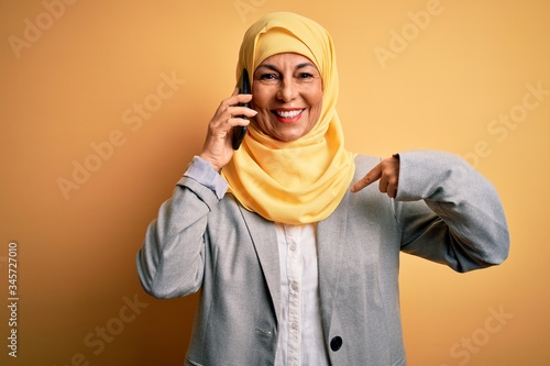 Middle age woman wearing traditional muslim hijab having conversation talking on smartphone with surprise face pointing finger to himself © Krakenimages.com