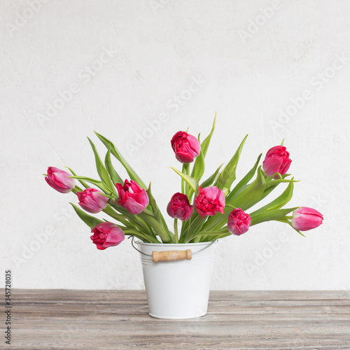 red tulips in bucket on background old white wall