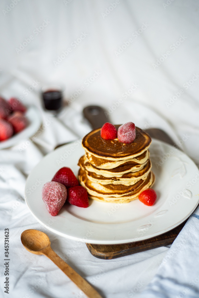 Close-up delicious pancakes, with strawberries and syrup on a light background. Sweet syrup flows from a stack of pancake Close-up delicious pancakes, with strawberries and syrup on a light background. Sweet syrup flows from a stack of pancake