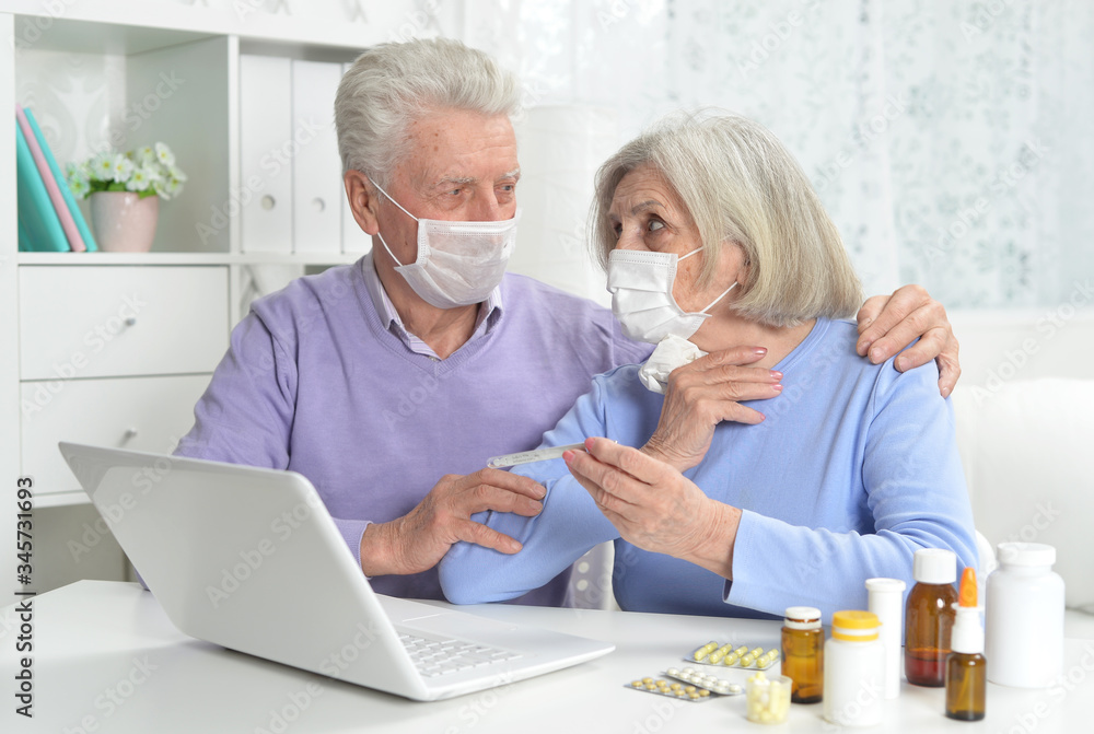 Ill senior couple with facial masks using laptop Ill senior couple with facial masks using laptop