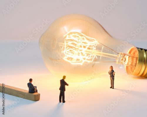 A businesswoman is lit by a large filament lightbulb (idea) as she presents to colleagues - Tiny People Working From Home