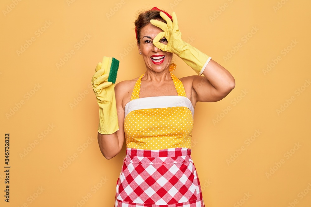 Middle age senior housewife pin up woman wearing 50s style retro dress using cleaner scrub with happy face smiling doing ok sign with hand on eye looking through fingers Middle age senior housewife pin up woman wearing 50s style retro dress using cleaner scrub with happy face smiling doing ok sign with hand on eye looking through fingers