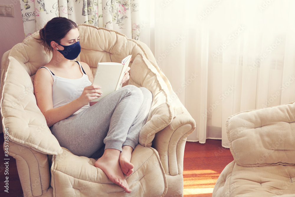 Woman reading book in protective mask, stay isolation at home for self quarantine. Concept home quarantine, prevention COVID-19, Coronavirus outbreak situation Woman reading book in protective mask, stay isolation at home for self quarantine. Concept home quarantine, prevention COVID-19, Coronavirus outbreak situation