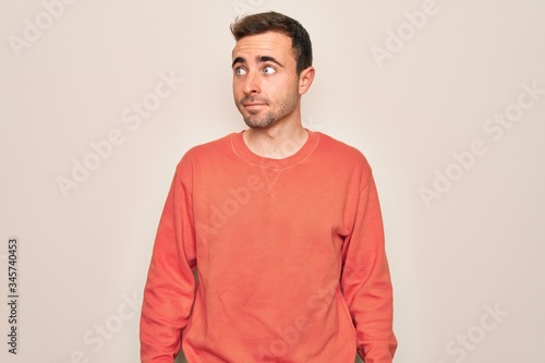 Young handsome man with blue eyes wearing casual sweater standing over white background smiling looking to the side and staring away thinking.