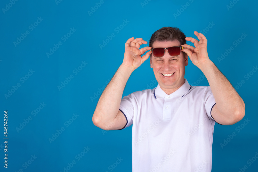 Close-up emotional portrait of a cheerful man in sunglasses. The man lifted his glasses from his eyes. Isolated on a blue background. Copy space for text. Close-up emotional portrait of a cheerful man in sunglasses. The man lifted his glasses from his eyes. Isolated on a blue background. Copy space for text.