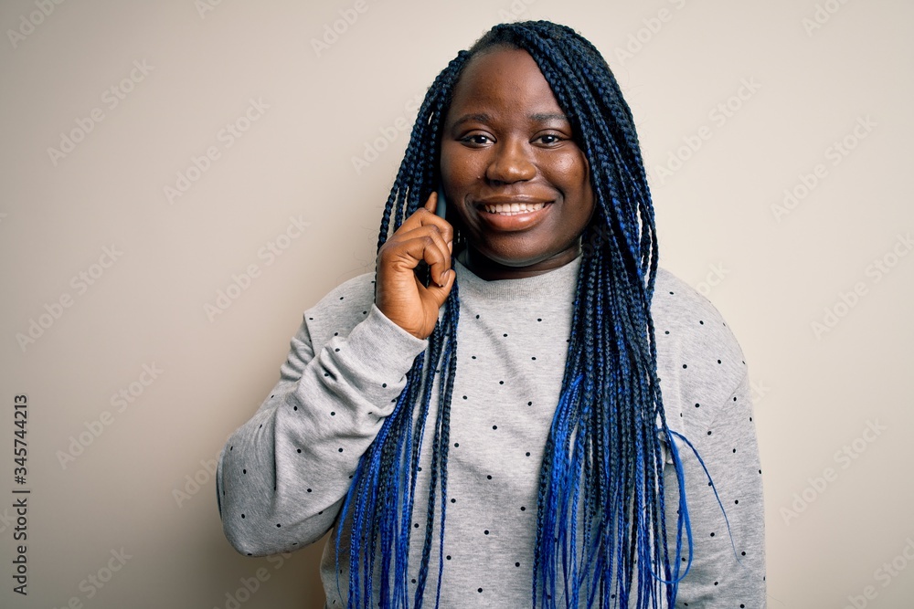 Young african american plus size woman with braids having conversation talking on smartphone with a happy face standing and smiling with a confident smile showing teeth Young african american plus size woman with braids having conversation talking on smartphone with a happy face standing and smiling with a confident smile showing teeth