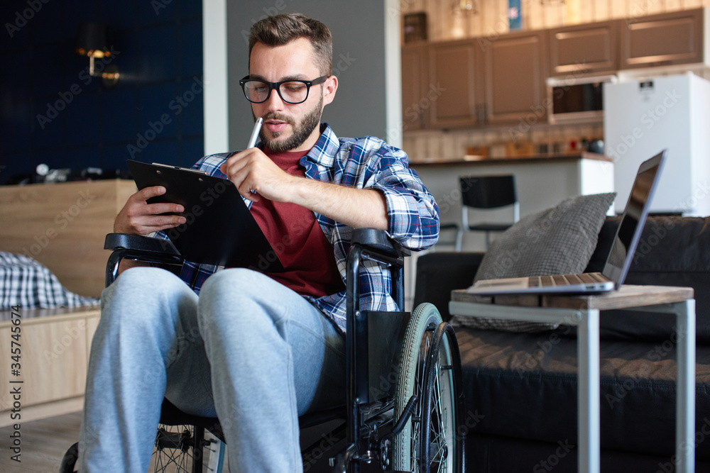 Disabled young man making notes in notepad while using laptop Disabled young man making notes in notepad while using laptop
