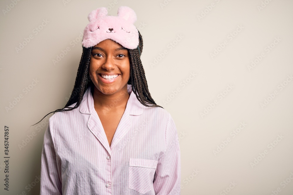 Young african american woman wearing pink pajama and sleep mask over isolated background with a happy and cool smile on face. Lucky person. Young african american woman wearing pink pajama and sleep mask over isolated background with a happy and cool smile on face. Lucky person.