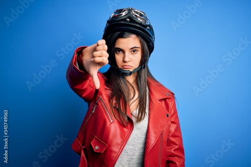 Young beautiful brunette motorcycliste woman wearing motorcycle helmet and jacket looking unhappy and angry showing rejection and negative with thumbs down gesture. Bad expression. © Krakenimages.com