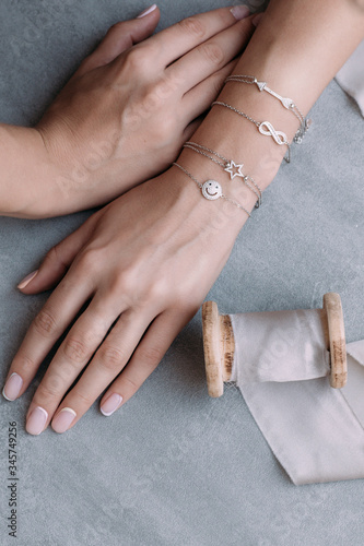 silver bracelets on a female hand on a gray background. on bracelets, decor in the form of arrows, infinity, star and smile. next to it is a silk ribbon reel photo