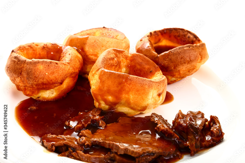 Traditional british meal of roast beef and yorkshire puddings with gravy on a white plate