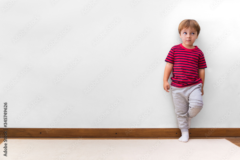 Boy with a rogue face and leaning against the wall. White background. Little child in his home. Copy space.