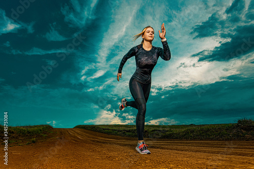 Workout outdoor. Sporty young woman and fit athlete runner running on the sky background. The concept of a healthy lifestyle and sport. Woman in black outfit.