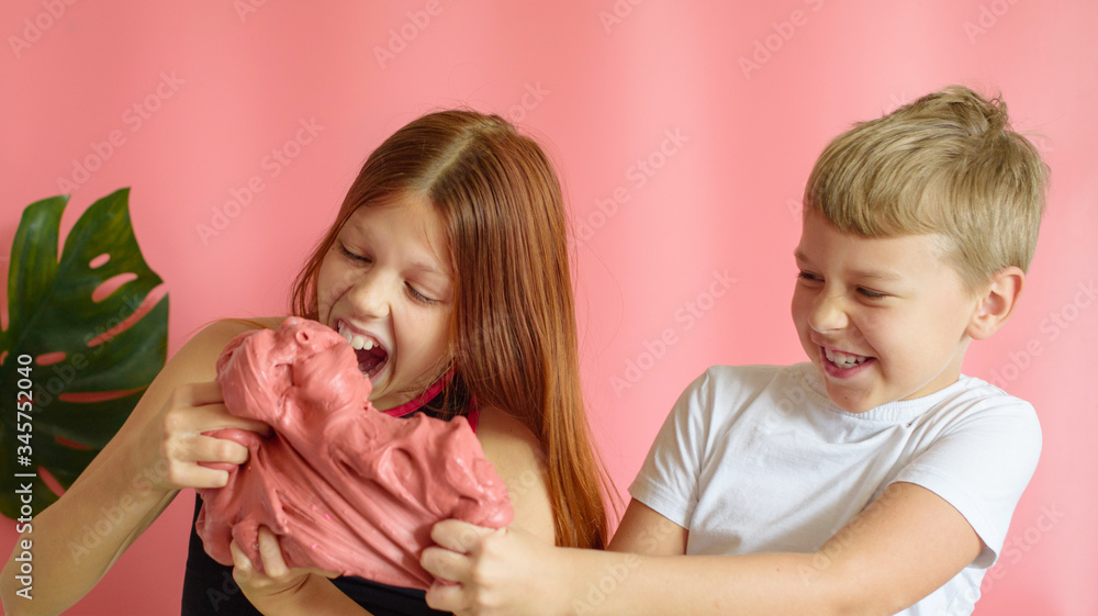 cute blonde boy and red hair girl playing with hand made slime on pink background cute blonde boy and red hair girl playing with hand made slime on pink background