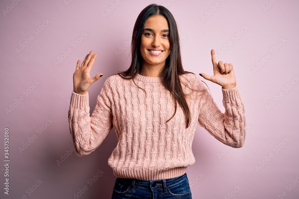 Young beautiful brunette woman wearing casual sweater over isolated pink background showing and pointing up with fingers number seven while smiling confident and happy. Young beautiful brunette woman wearing casual sweater over isolated pink background showing and pointing up with fingers number seven while smiling confident and happy.